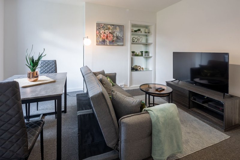 Modern living room with grey sofa, TV, shelving, dining table and plant decor