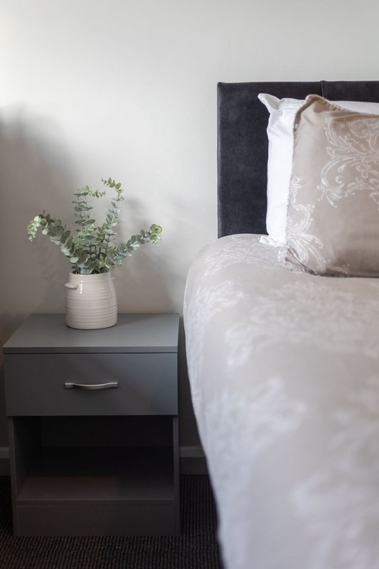 Bedroom with double bed, dark headboard, white bedding, and bedside table with potted plant