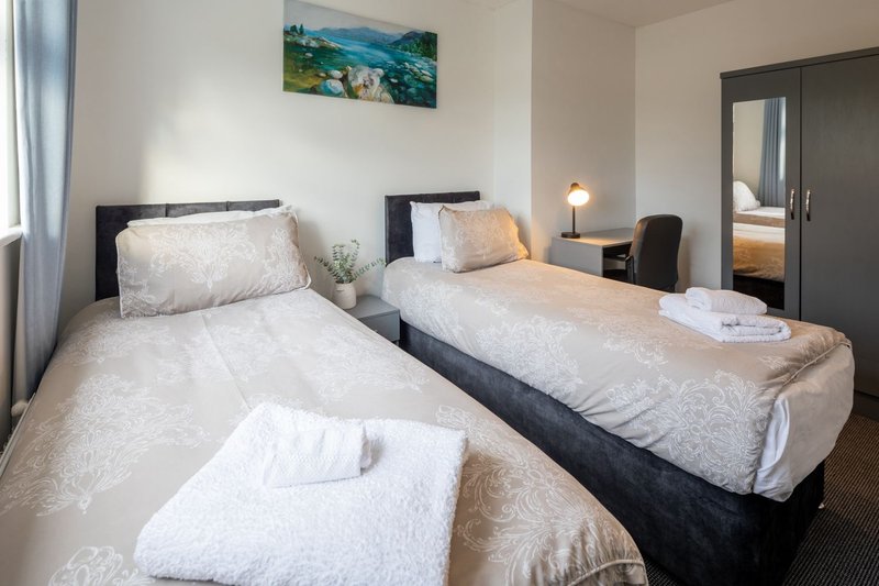 Bright bedroom with three single beds, white bedding, landscape artwork and en-suite visible