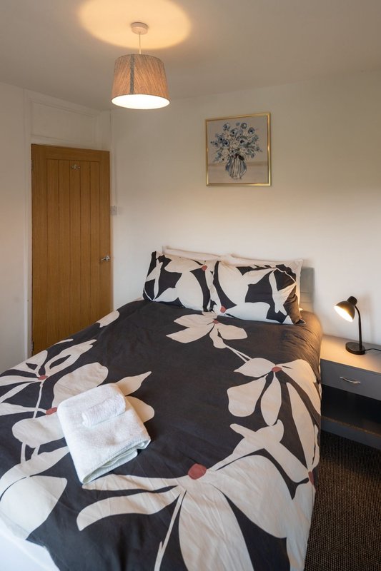 Bedroom with double bed, patterned bedding, wooden door, ceiling light and framed wall art