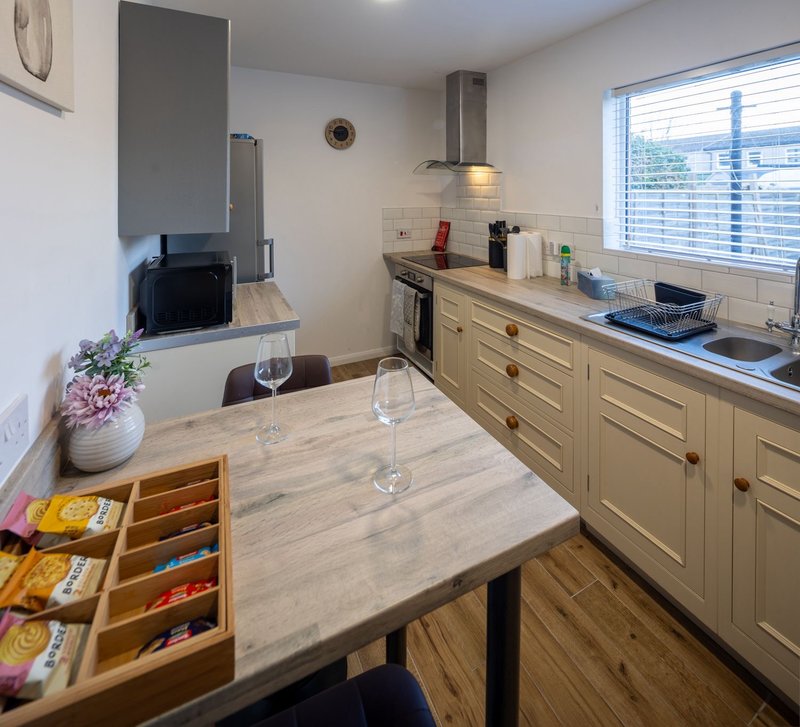 Modern kitchen with cream cabinetry, dining table, potted flowers and windows overlooking garden