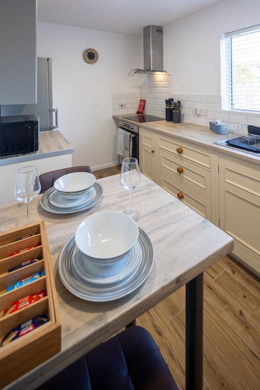 Modern kitchen with cream cabinetry, island table set with place settings, and stainless steel cooker hood