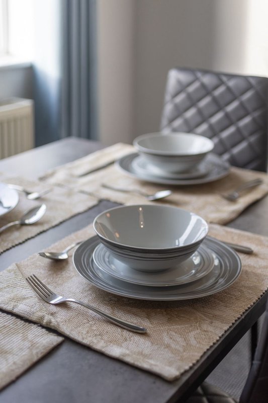Dining table set with grey plates, cutlery, and napkins, with upholstered chair visible