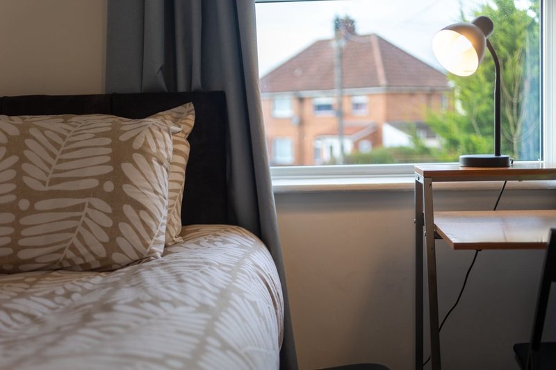 Bedroom with patterned bedding, cushion, window view of brick building and garden