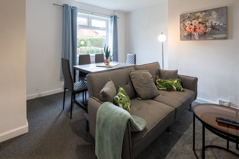 Living room with brown sofa, desk, chair, window with curtains and potted plants