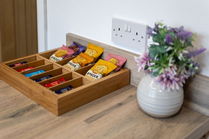 Kitchen counter with tea organizer, white electrical outlet, and white vase of purple flowers