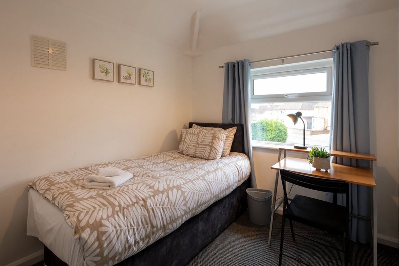 Bright bedroom with single bed, desk, chair, window with grey curtains and framed wall art