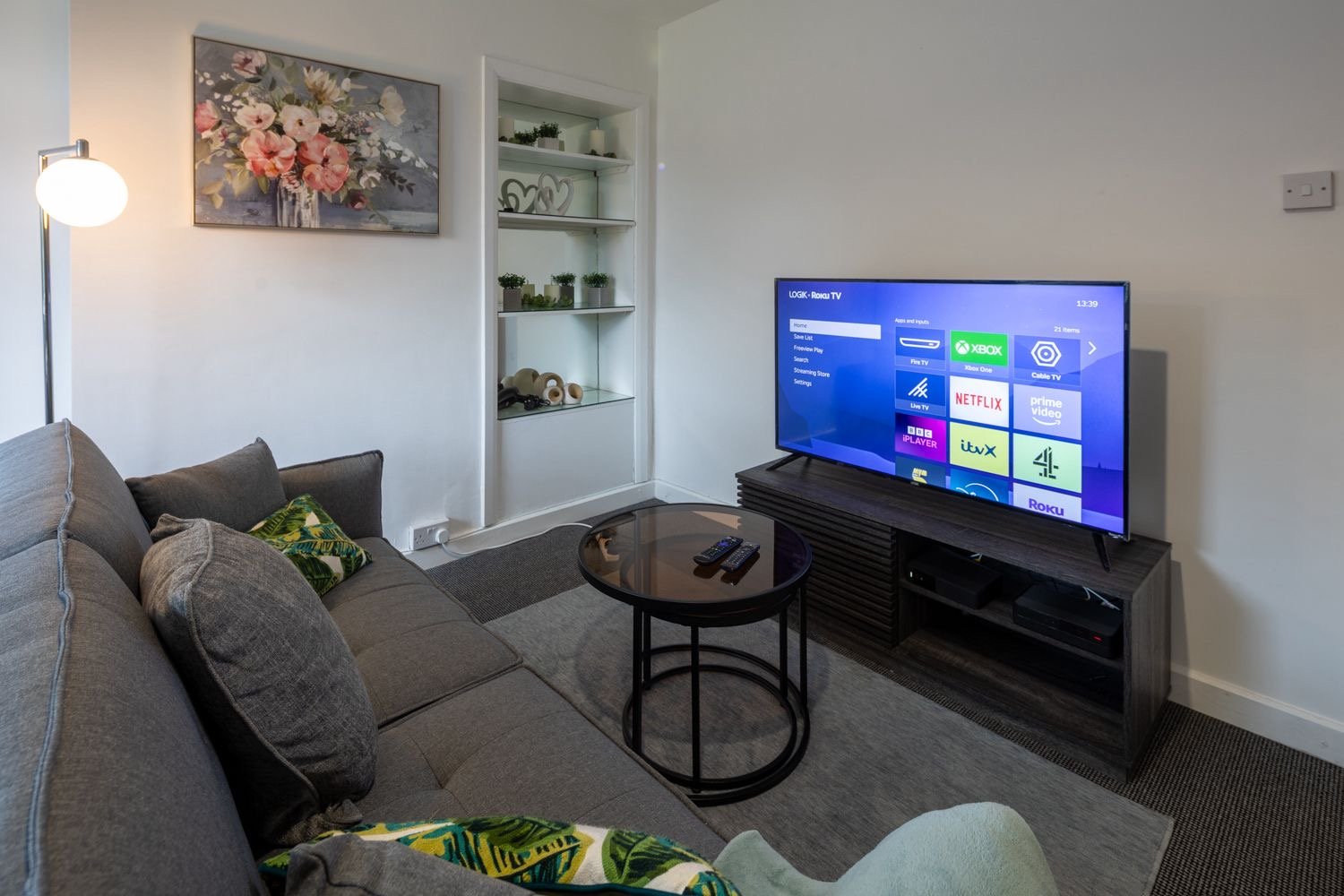 Modern living room with grey sofa, smart TV, round side table and wall shelving
