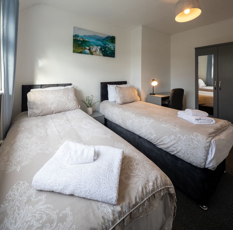 Triple bedroom with three single beds, white bedding, black frames, landscape artwork and pendant lighting