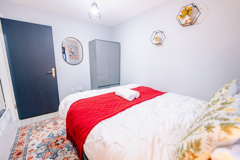 Bright bedroom with double bed, red throw, white bedding, dark blue door and geometric wall decor