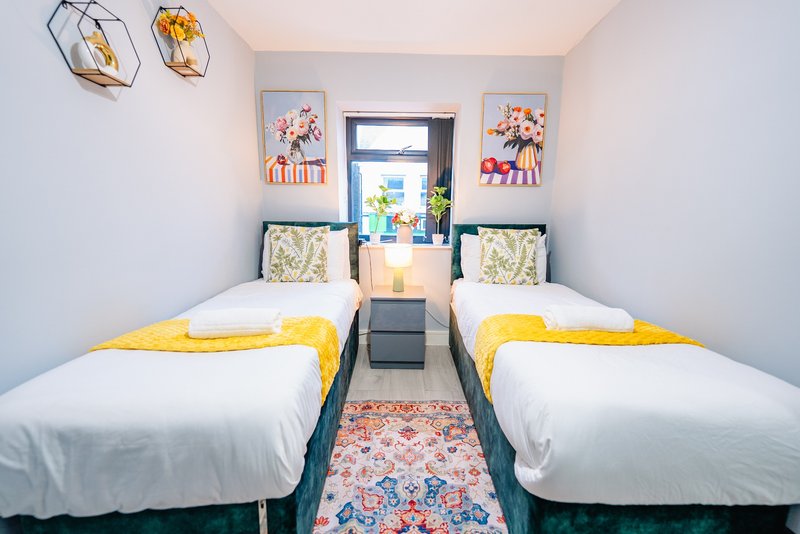 Twin bedroom with two single beds, yellow bedding, framed artwork and window with natural light