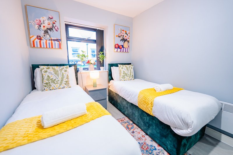 Twin bedroom with two single beds, yellow throws, patterned cushions and framed wall art