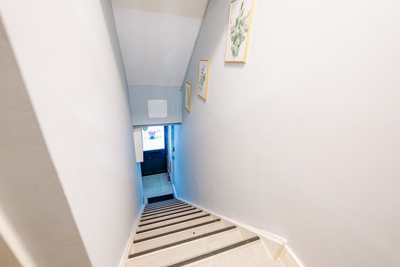 Narrow staircase with wooden steps descending to blue-painted lower level, white walls