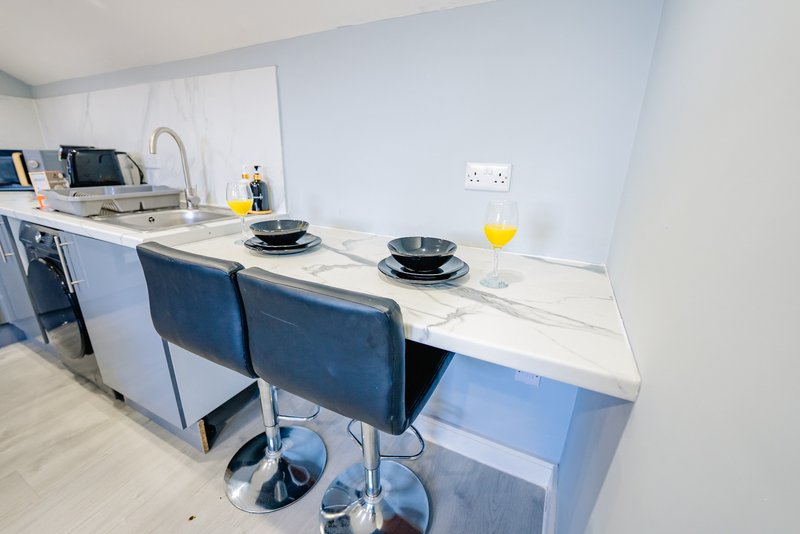 Modern kitchen with white countertop, bar seating, blue chairs, and stainless steel sink