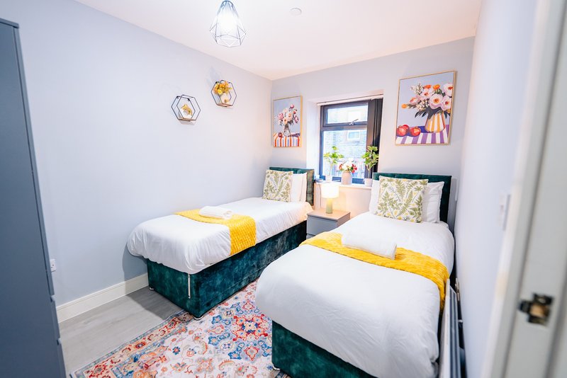 Bright twin bedroom with two single beds, yellow accents, floral rug and wall art