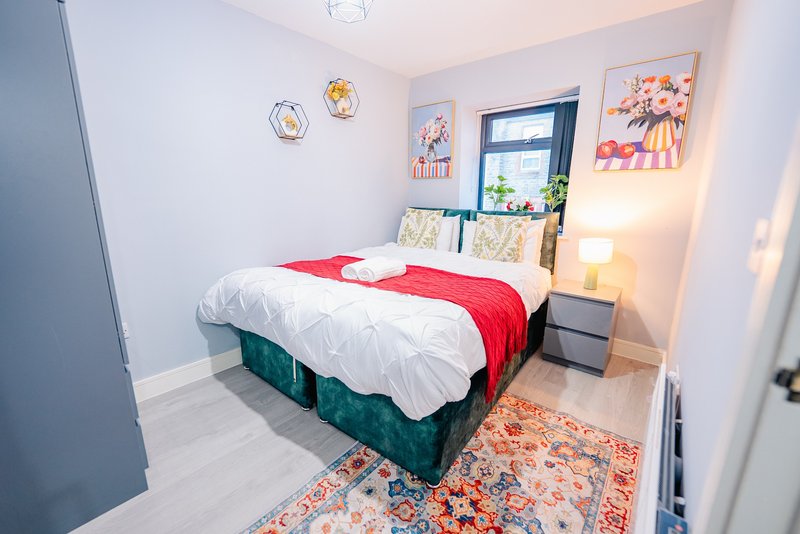 Modern bedroom with double bed, red throw, white bedding, window with plants, wall art and bedside lamp
