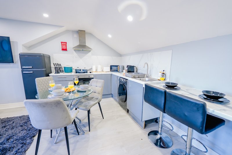 Modern open-plan kitchen and dining area with blue cabinetry, dining table, and stainless steel appliances
