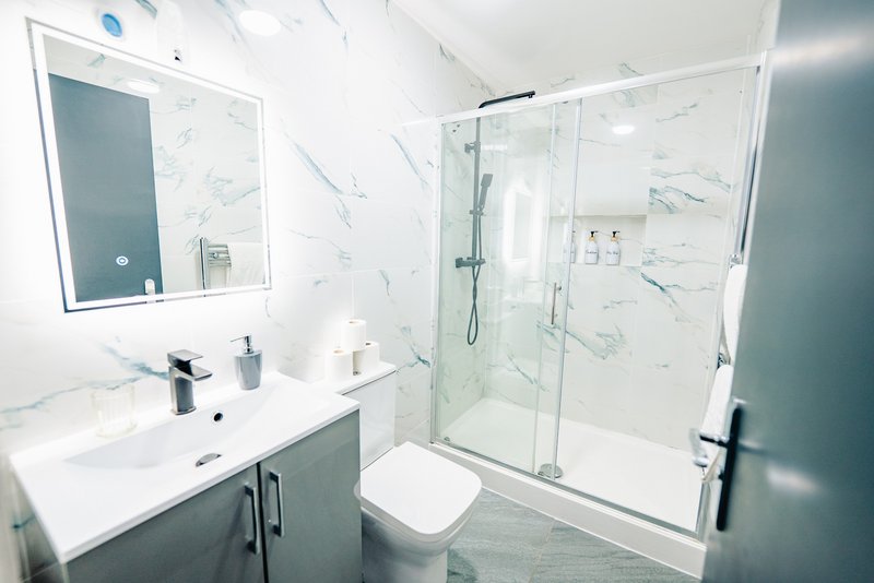 Modern bathroom with marble-effect tiles, white sink, mirror, toilet and glass shower enclosure