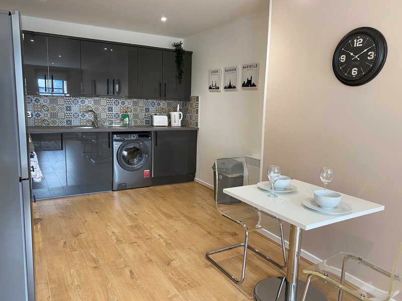 Modern kitchen with black cabinetry, washing machine, wooden flooring and dining table