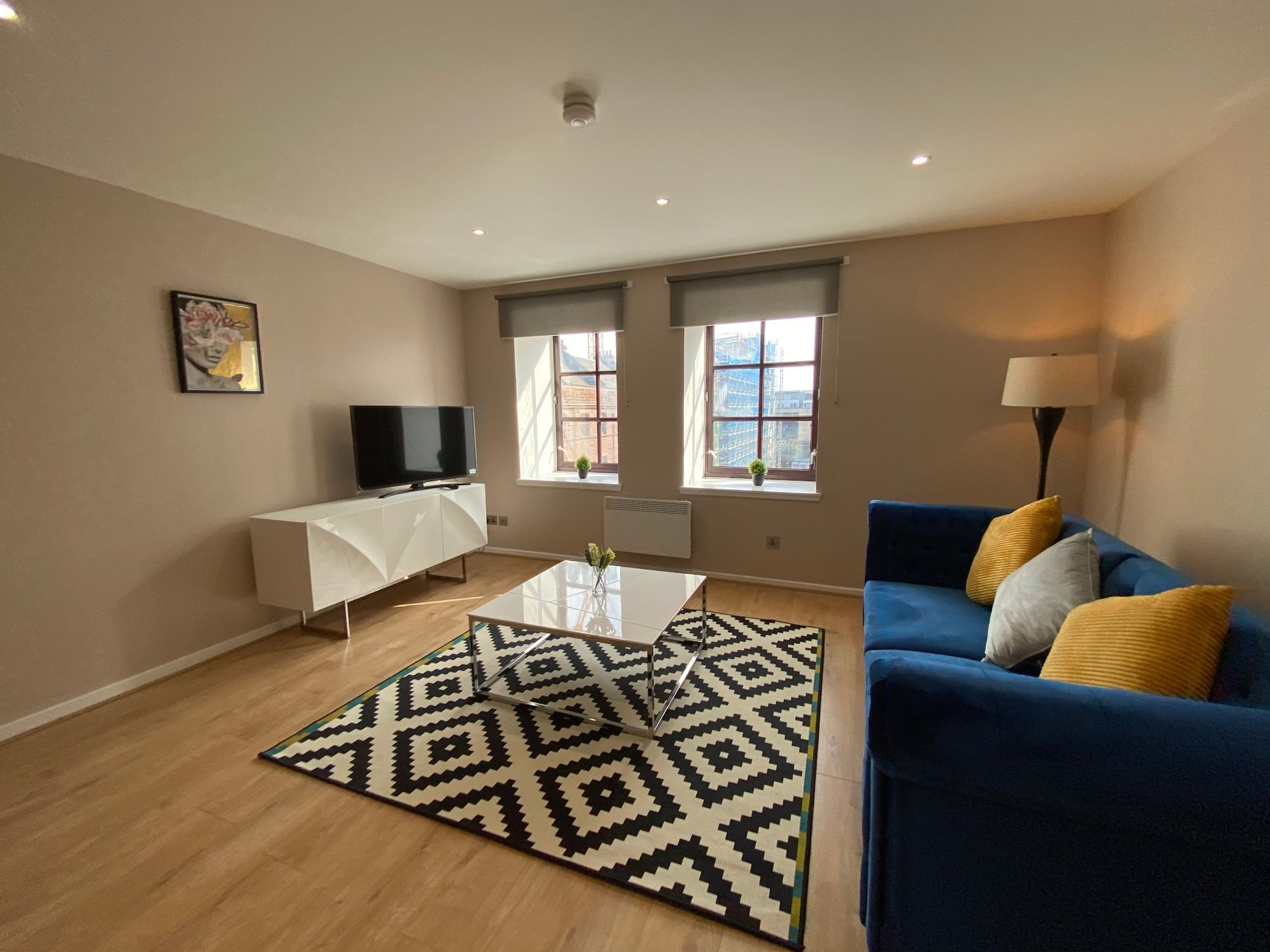 Modern living room with blue sofa, geometric rug, TV unit, and large windows
