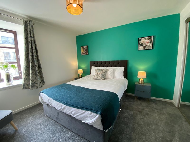 Modern bedroom with double bed, teal accent wall, bedside lamps and window