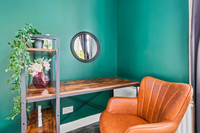 Teal bedroom corner with orange leather chair, wooden desk, shelving unit with plants and flowers