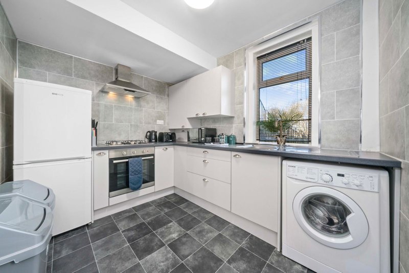 Modern kitchen with white cabinetry, integrated appliances, washing machine, and window view