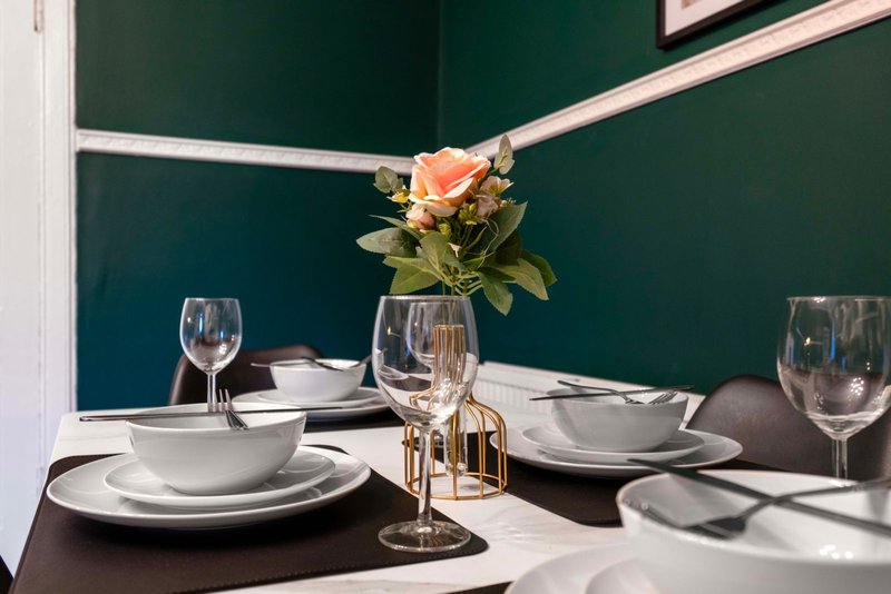 Formal dining table set with white plates, glasses, and peach flower centerpiece against green wall