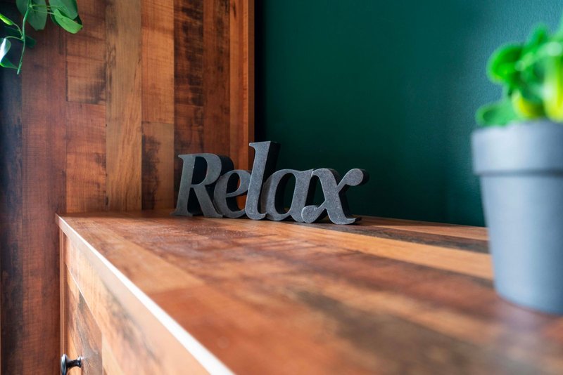 Wooden desk with decorative 'Relax' sign and potted plant against teal wall