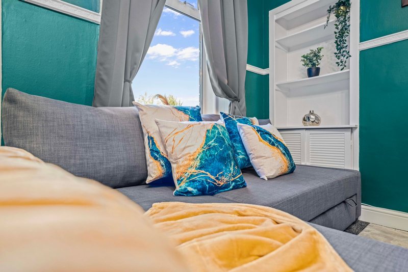 Bright bedroom with grey sofa, teal accent wall, decorative cushions and window with countryside view