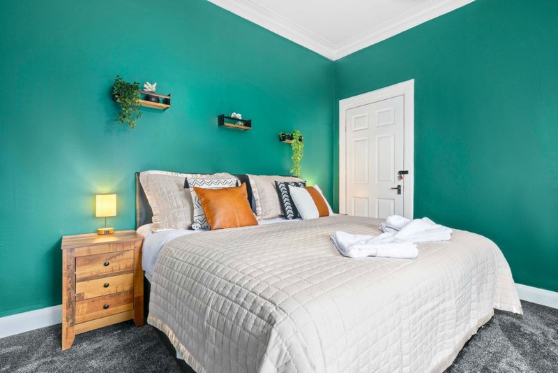 Bright bedroom with turquoise walls, double bed with white bedding, wooden nightstand and lamp