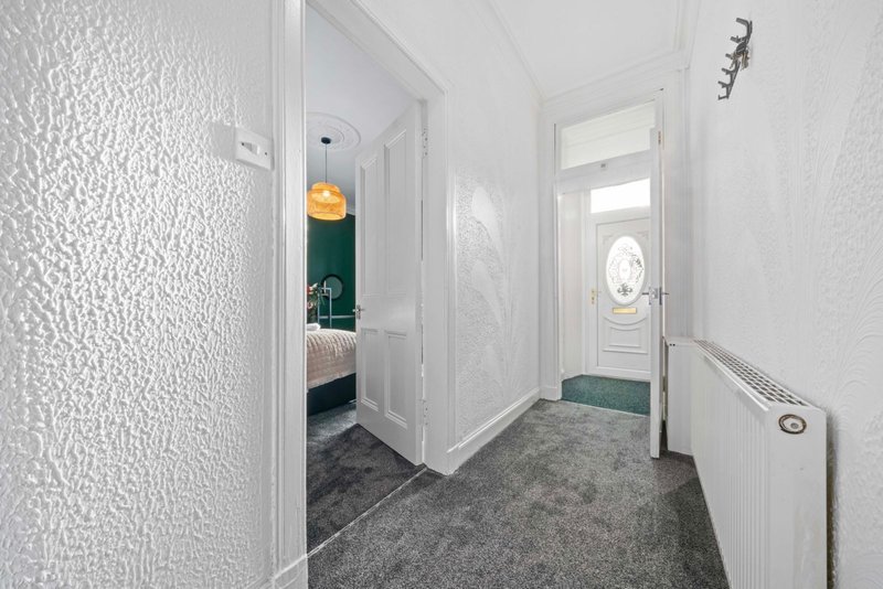 Bright hallway with white walls, gray carpet, doors leading to bedroom and entrance