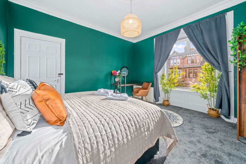 Modern bedroom with teal walls, double bed, orange accent pillows and pendant lighting
