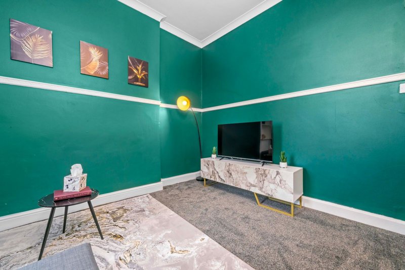 Modern living room with teal walls, TV unit, small side table and framed artwork