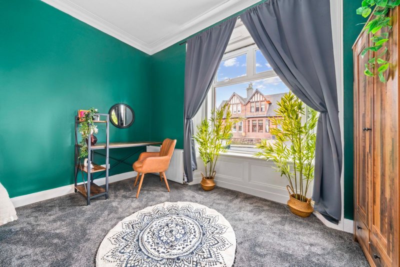 Bright bedroom with turquoise walls, orange chair, grey carpet and large window overlooking street