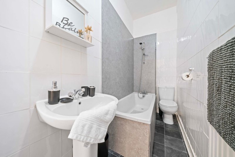 Modern bathroom with white sink, shower enclosure, toilet, and tiled walls