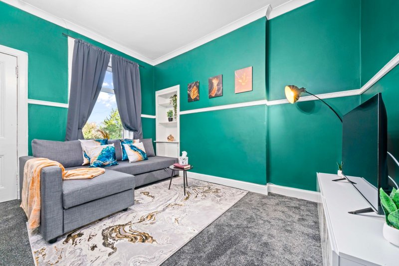 Bright living room with teal walls, grey sofa, white shelving and floor lamp