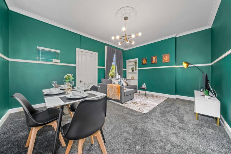 Bright green open-plan living space with dining table, black chairs, sofa and white shelving