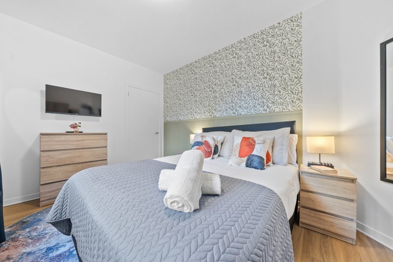 Modern bedroom with queen bed, wooden nightstands, textured accent wall and wall-mounted TV