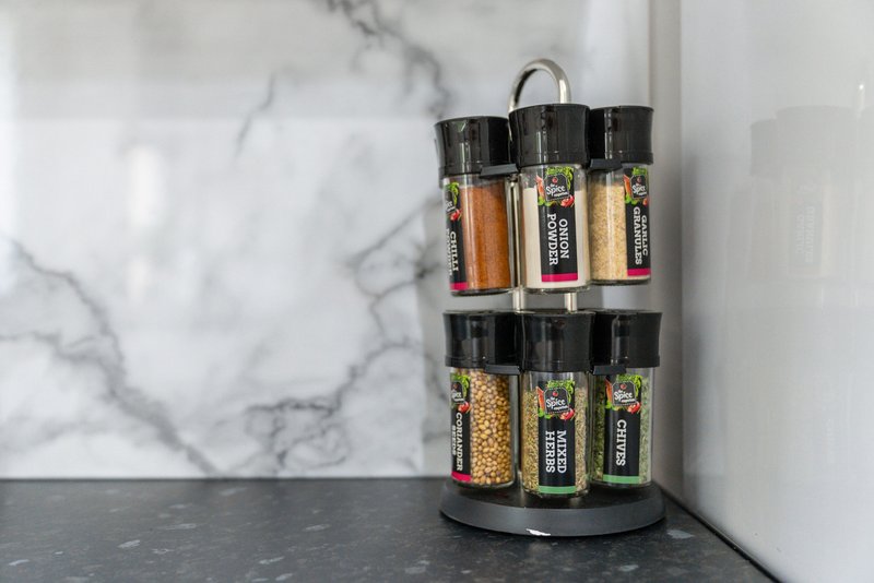 Kitchen counter with rotating spice rack containing labeled glass jars and marble backsplash
