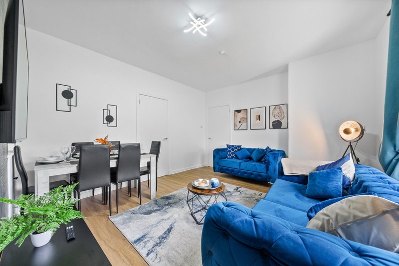 Open-plan living and dining area with blue sofa, dining table, wooden flooring and wall art