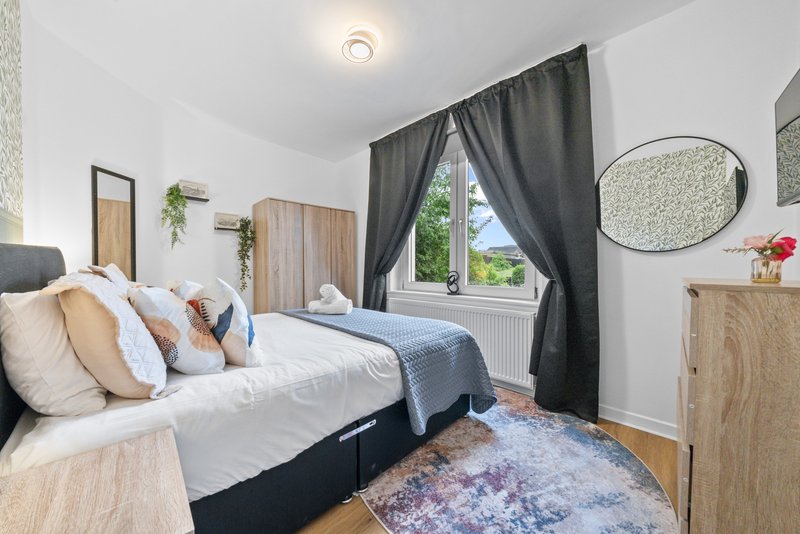 Bright bedroom with double bed, wooden furniture, dark curtains and round mirror