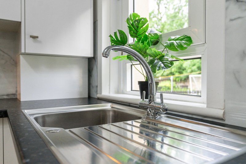 Modern kitchen sink with chrome faucet, stainless steel drainboard, and potted plant by window