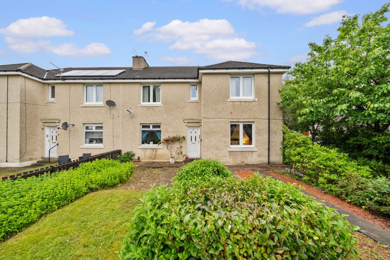 Cream-colored terraced house with front garden, lawn and shrubs, blue sky
