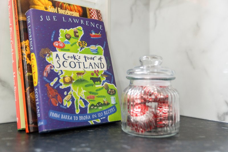 Kitchen shelf with stack of books, glass jar with red and white candies, marble backsplash