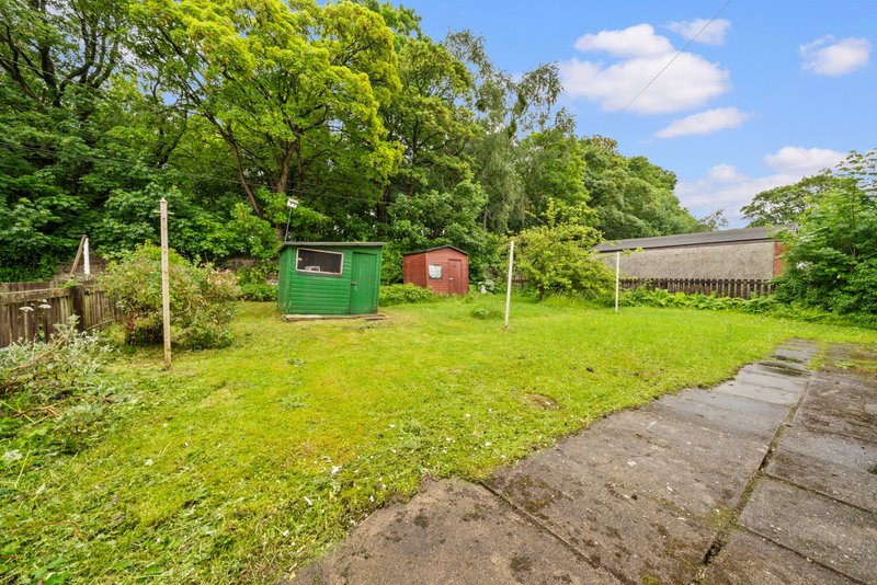 Garden area with green lawn, storage sheds, concrete path and surrounding trees