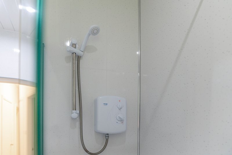 Bathroom shower with white electric heater unit and handheld showerhead