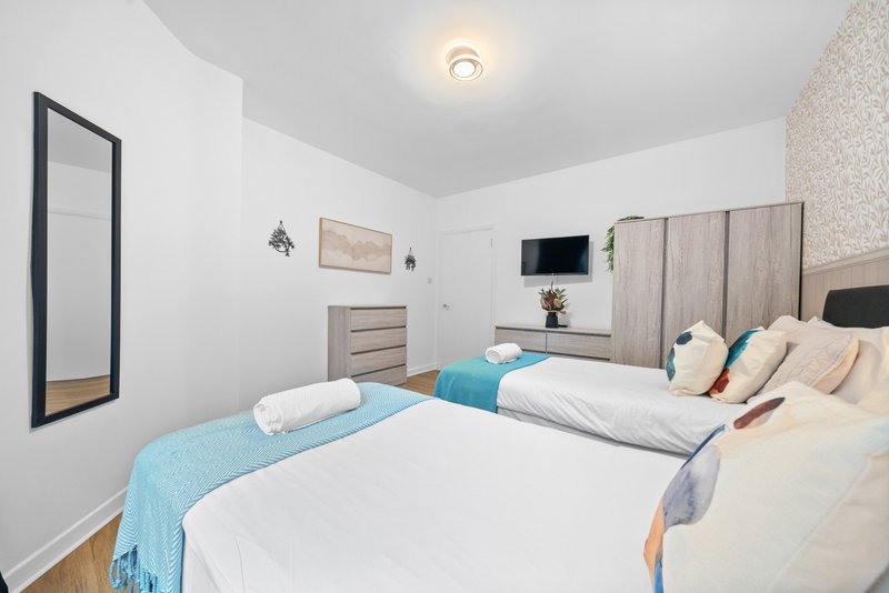 Modern bedroom with two double beds, headboard, wall-mounted TV, mirror and neutral décor