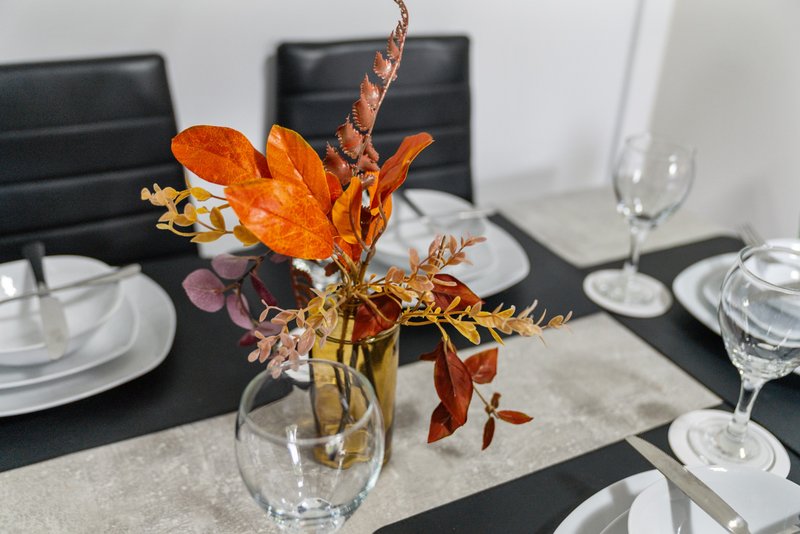 Dining table set with autumn floral arrangement in glass vase and place settings