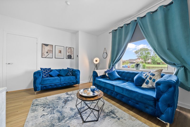 Bright living room with two blue velvet sofas, wooden floor, teal curtains and garden view
